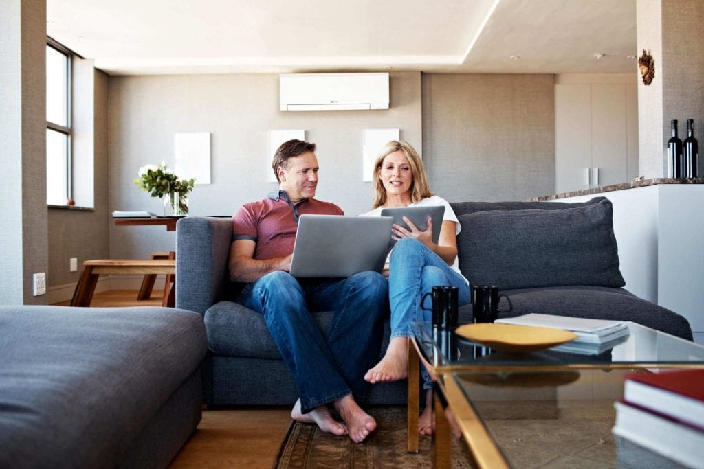 Couple sitting on couch enjoying the added comfort of ductless mini-split heat pump. 