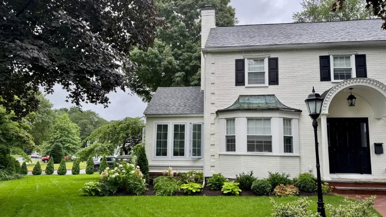 1938 colonial home in Worcester, Massachusetts with a ducted heat pump installed to the left side of the home.