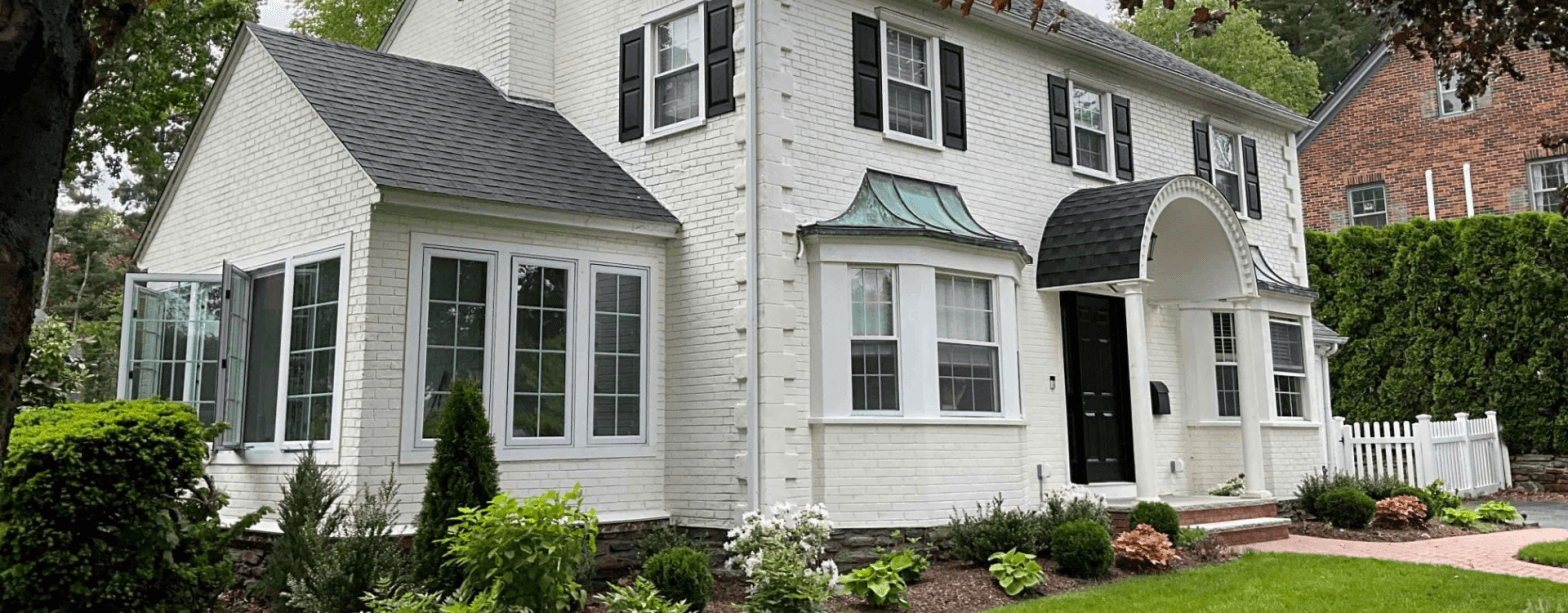 Outside of 1939 Colonial home in WOrcester, Massachusetts with a lushes garden and central heat pump located on the left side of the home.