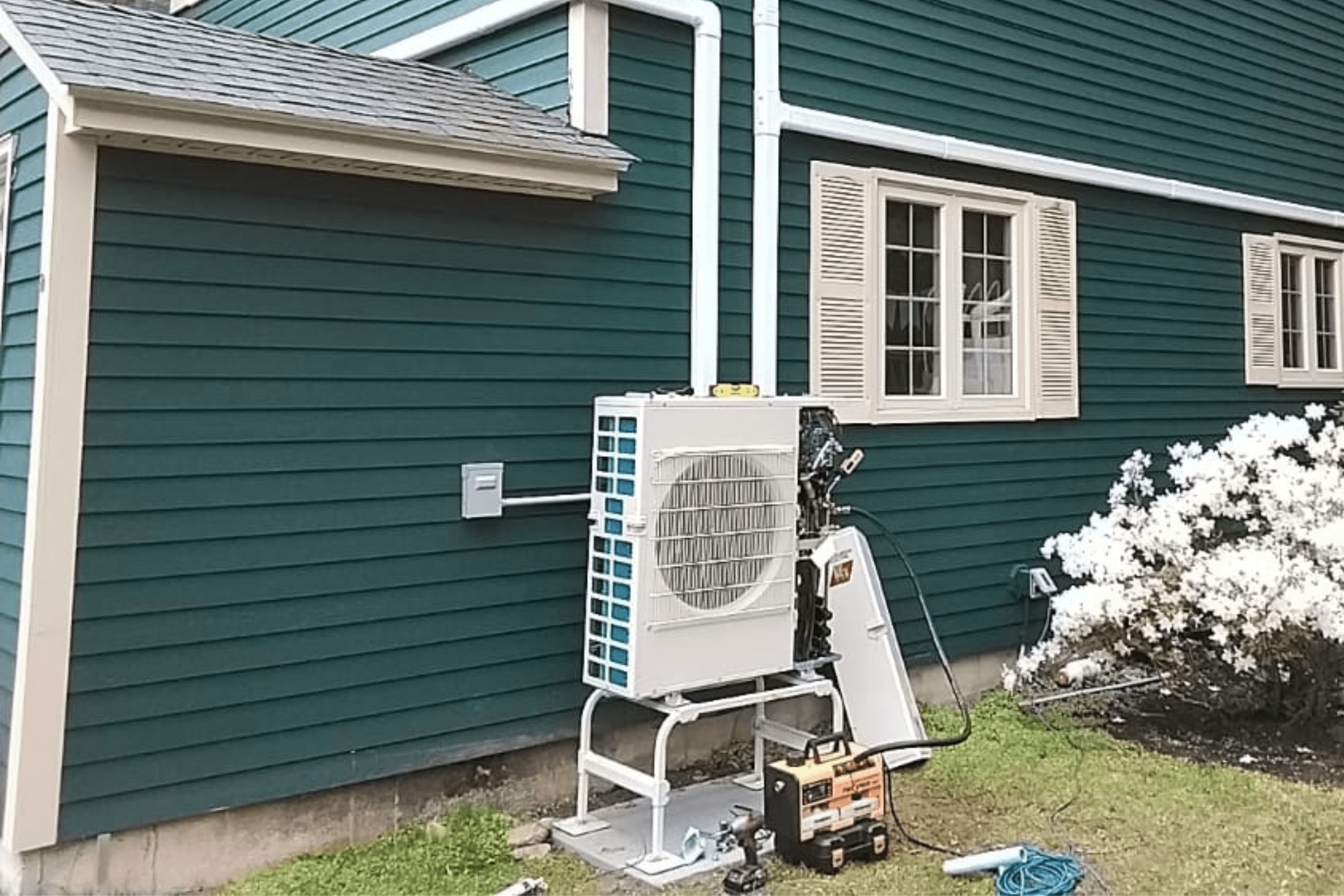 Outside green home in Leominster, Massachusetts> Mitsubishi condenser is located on side of the house.